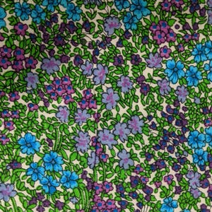 May include: Close-up of a floral fabric pattern. The design features small blue, purple, and pink flowers with green leaves on a cream background. The flowers are densely packed, creating a vibrant and colorful textile.