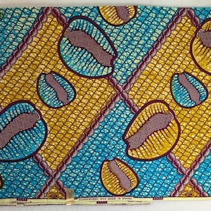 May include: A vibrant fabric with a repeating pattern of large, oval shapes in teal, yellow, and burgundy. The design is set against a grid-like background, with diagonal lines of burgundy beads. The fabric has a tag that reads "GUARANTEED WAX MADE IN GHANA."