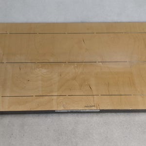 Könnte beinhalten: Ein hellbraunes Holzbrett mit einem Rastermuster aus in die Oberfläche geätzten Linien. Das Brett ist etwa 46 cm breit und 91 cm lang.