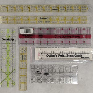 May include: Assortment of clear plastic quilting rulers with black markings. The rulers include Omnigrid, Creative Grids, and Quilter's Rule Seam Guide. The rulers are in various sizes and have different markings for quilting.