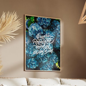 Puede incluir: Un cuadro enmarcado con un primer plano de flores de hortensia azules. La obra de arte incluye una escritura blanca que dice "Quiero Regalarte Azul de los Dias". La impresión se muestra en una pared marrón.
