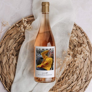 Op de afbeelding: Een fles ros&eacute; wijn met een gepersonaliseerd etiket. Het etiket bevat een foto van een persoon die een geel sweatshirt draagt met rode harten en de tekst "Wil je mijn bruidsmeisje zijn?" De tekst "Savannah" is in cursief geschreven onderaan het etiket.