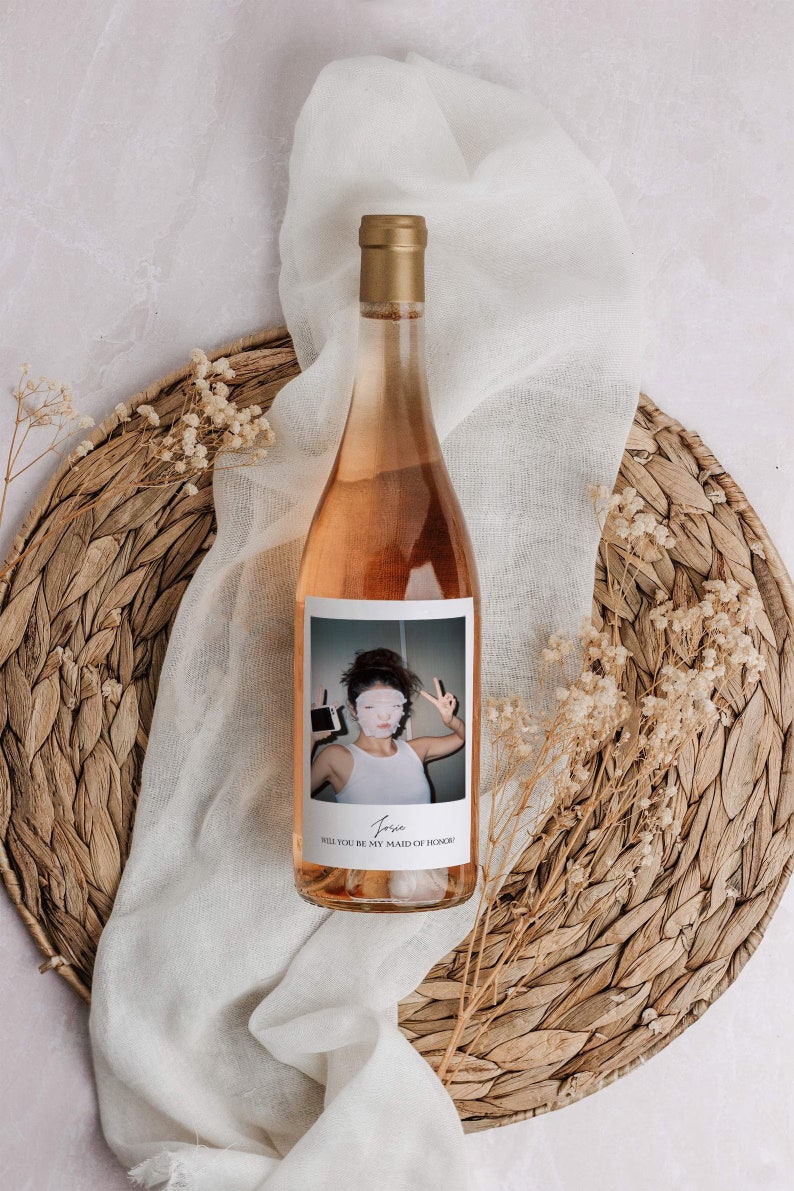 Op de afbeelding: Een fles ros&eacute; wijn met een gepersonaliseerd etiket met een foto van een vrouw en de tekst "Josie, Wil je mijn bruidsmeisje zijn?"