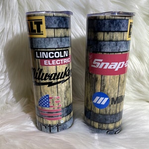 May include: Two stainless steel tumblers with a wood grain design. The tumbler on the left has the text "Lincoln Electric Milwaukee" and an American flag. The tumbler on the right has the text "Snap-on" and "Miller".