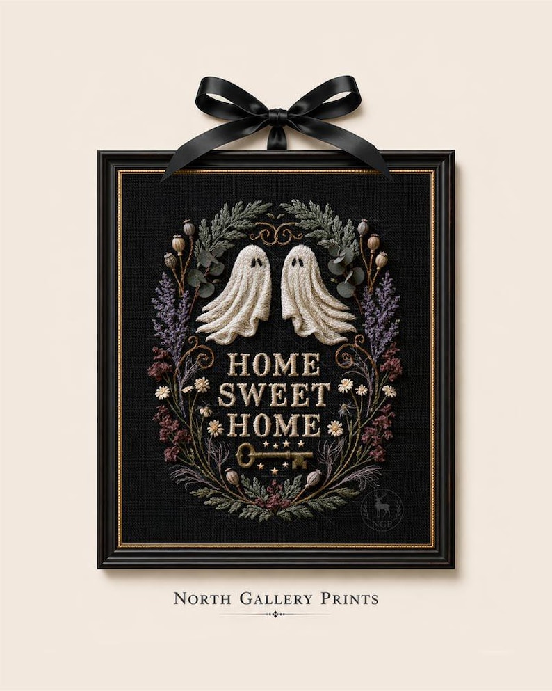 May include: A framed embroidery piece on black fabric featuring two white ghosts, a floral wreath, and the text "HOME SWEET HOME" with a key icon. The rectangular black frame is topped with a black satin ribbon bow. The design includes botanical elements.