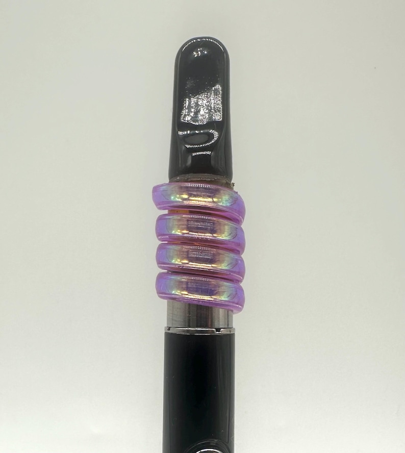 May include: A black vape pen with a purple iridescent glass mouthpiece. The mouthpiece is made of several rings that are stacked on top of each other.