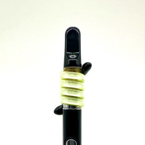 May include: A black vape pen with a green silicone sleeve. The sleeve is made up of multiple rings that are stacked on top of each other.