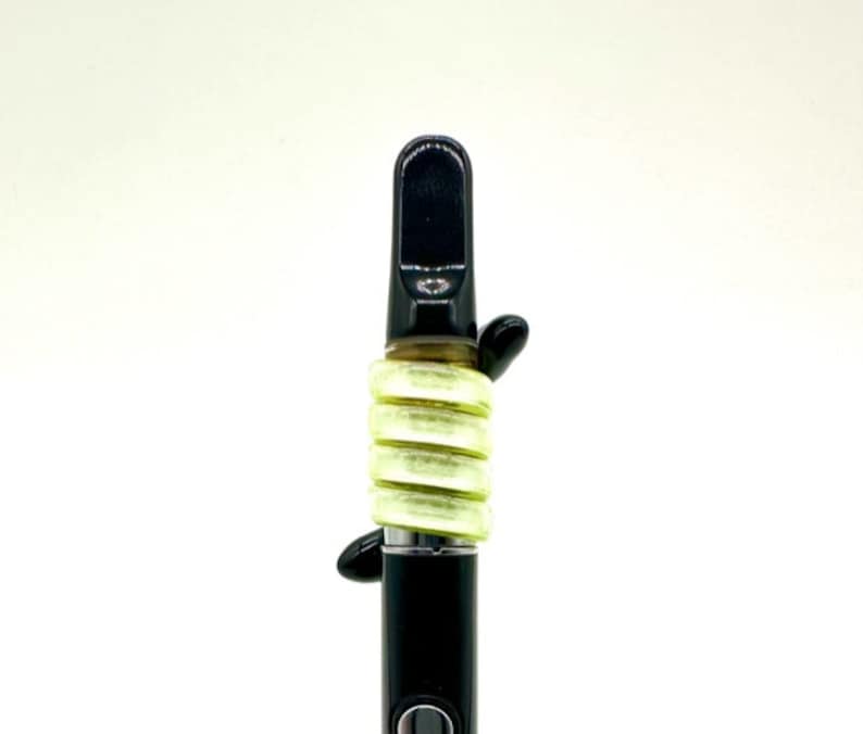 May include: A black vape pen with a green silicone sleeve. The sleeve is made up of multiple rings that are stacked on top of each other.