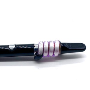 May include: A black and silver vape pen with a purple and white silicone sleeve. The sleeve is made up of multiple rings that are stacked on top of each other.