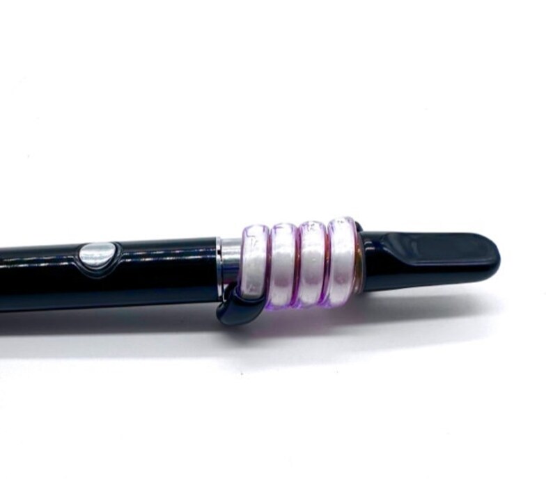 May include: A black and silver vape pen with a purple and white silicone sleeve. The sleeve is made up of multiple rings that are stacked on top of each other.