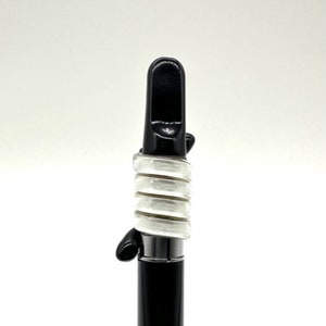 May include: A black and white vape pen with a mouthpiece and a white silicone sleeve.