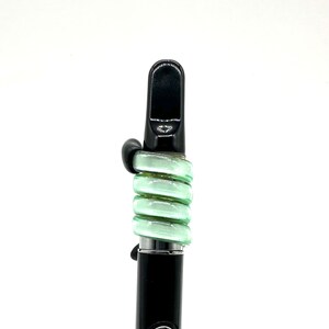 May include: A black and green vape pen with a mouthpiece and a coil of green glass around the middle.