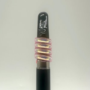 May include: A black and silver vape pen with a pink iridescent glass mouthpiece. The mouthpiece is made of multiple rings that are stacked on top of each other.