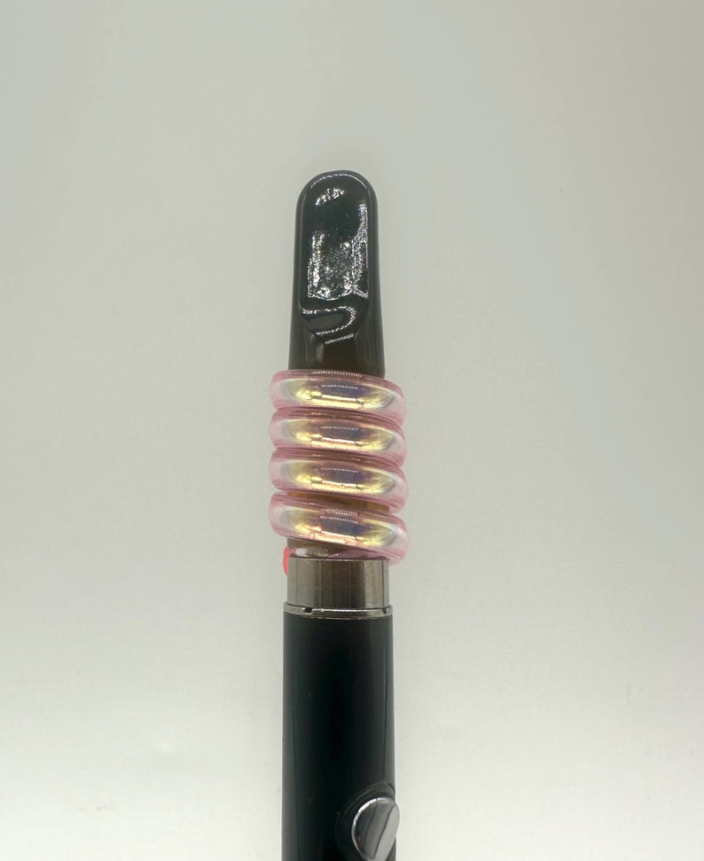 May include: A black and silver vape pen with a pink iridescent glass mouthpiece. The mouthpiece is made of multiple rings that are stacked on top of each other.