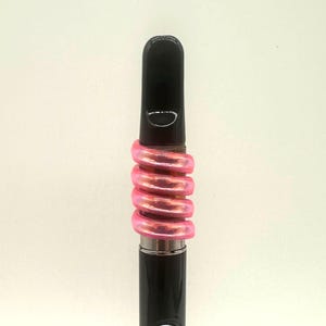May include: A black vape pen with a pink iridescent silicone band around the middle.