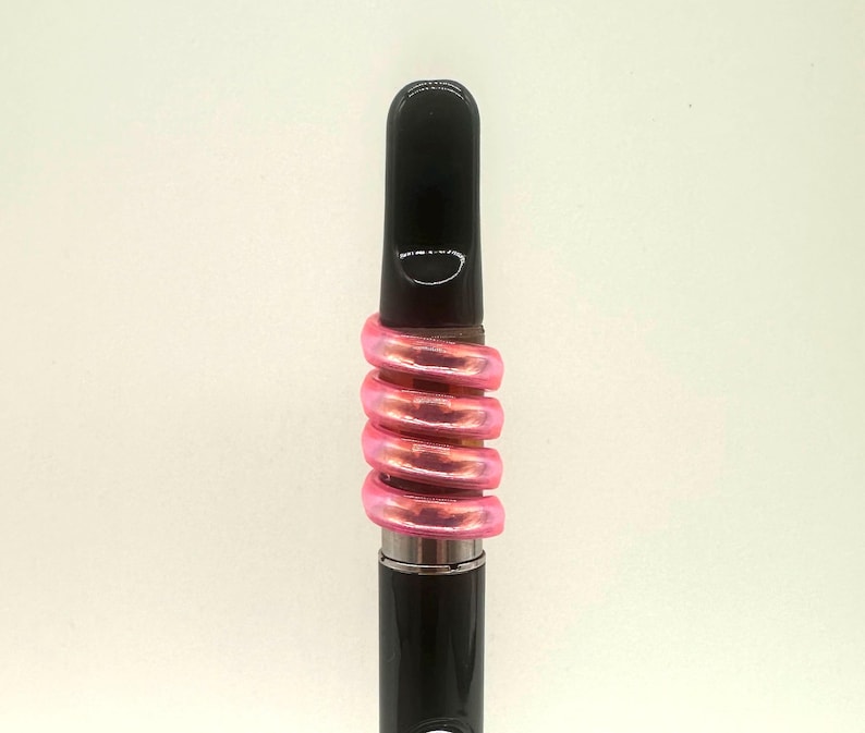 May include: A black vape pen with a pink iridescent silicone band around the middle.
