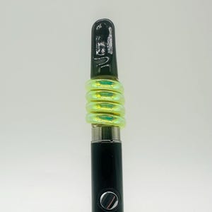 May include: A black vape pen with a green iridescent silicone sleeve. The sleeve is made up of multiple rings.
