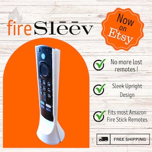 May include: White stand for a black Fire TV Stick remote. The stand is shaped like a pedestal with a rounded base. The stand is designed to hold the remote upright. The text "No more lost remotes!" is visible in the image. The text "Sleek Upright Design" is visible in the image. The text "Fits most Amazon Fire Stick Remotes" is visible in the image. The text "FREE SHIPPING" is visible in the image.