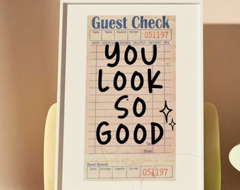 May include: A framed print of a vintage-style guest check with the text "you look so good" written in black marker. The print is hanging on a wall above a yellow couch.