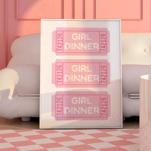 May include: A white framed print with three pink tickets that say "Girl Dinner" and the number "7422126" on each ticket. The print is hanging on a pink wall above a white sofa.