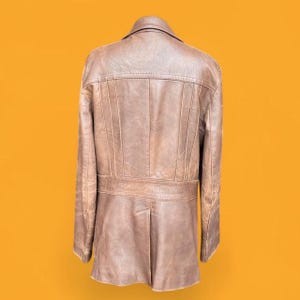 May include: A brown leather jacket shown from the back, featuring a structured collar, vertical seam detailing across the upper back, and a horizontal waistband panel. The garment has long sleeves and a straight hemline with a central back vent.