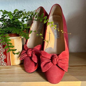 May include: A pair of red suede shoes with a bow on the front. The shoes are labelled "Laura Ashley" and "Made in Italy".