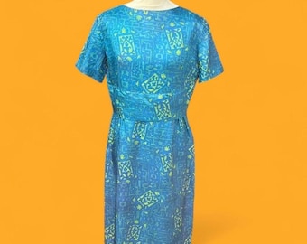 May include: A knee-length dress featuring a vibrant blue base with a repeating geometric pattern in lime green. The garment has short sleeves, a round neckline, and a fitted waistline, displayed on a mannequin against a solid orange background.