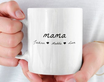 Könnte beinhalten: Weiße Keramiktasse mit dem Wort "mama" in Kursivschrift und den Namen "Jackson", "Maddie" und "Liam" darunter geschrieben, mit einem Herzsymbol zwischen jedem Namen.