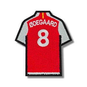 May include: Embroidered patch of a red soccer jersey with white accents. The jersey features the name "ØDEGAARD" above the number "8" in white. The patch has a black border and a yellow stripe at the collar.
