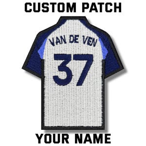 May include: Custom patch in the shape of a jersey. The patch is white with blue accents and features the name "VAN DE VEN" and the number "37" in blue. The text "CUSTOM PATCH" and "YOUR NAME" are above and below the jersey.