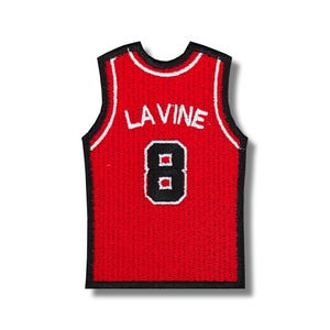 Puede incluir: Camiseta de baloncesto roja con ribetes negros y letras blancas. La camiseta tiene el nombre "LAVINE" y el número "8" en la espalda.