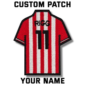 Puede incluir: Un parche personalizado con forma de camiseta de fútbol. La camiseta es de rayas rojas y blancas con el nombre "RIGG" y el número "11" en negro. El parche tiene el texto "CUSTOM PATCH" y "YOUR NAME" en negro.
