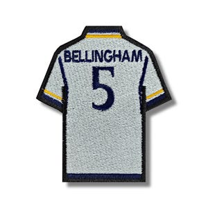 May include: White football shirt patch with blue and yellow trim. The back of the shirt has the name "BELLINGHAM" and the number "5" in blue.