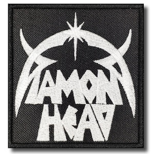 May include: A square, black patch with white embroidered text and design. The text reads "DIAMOND HEAD" in a stylized font, with a star and curved lines above. The patch has a black border.