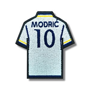 May include: White soccer jersey patch with blue and yellow trim. The back of the jersey has the name "MODRIC" and the number "10" in blue.