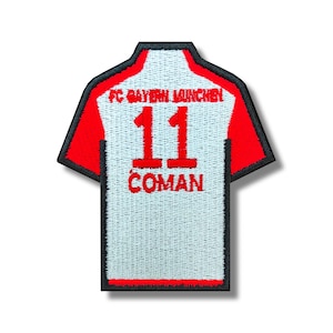 Peut inclure: Patch brodé blanc et rouge d'un maillot de football avec le numéro 11 et le nom "COMAN" au dos. Le texte "FC BAYERN MÜNCHEN" est visible en haut du patch.