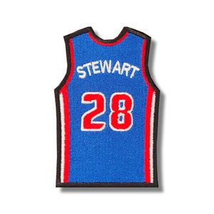 Könnte beinhalten: Blauer Basketballtrikot-Patch mit weißen und roten Rändern. Auf der Rückseite des Trikots steht der Name "STEWART" und die Nummer "28" in Rot.