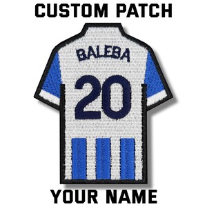 Op de afbeelding: Aangepaste patch in de vorm van een voetbalshirt. Het shirt is wit met blauwe accenten, de naam "BALEBA" en het nummer "20" in marineblauw. De tekst "CUSTOM PATCH" en "YOUR NAME" staan boven en onder het shirt.