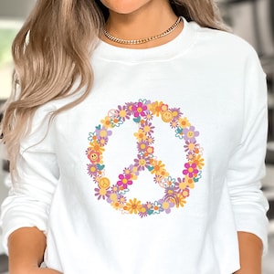 May include: White sweatshirt with a peace sign made of colorful flowers and smiley faces.