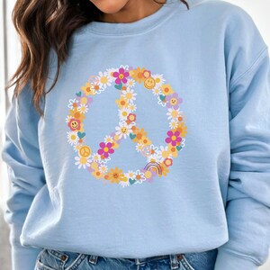 May include: A light blue sweatshirt with a peace sign made of flowers and smiley faces.