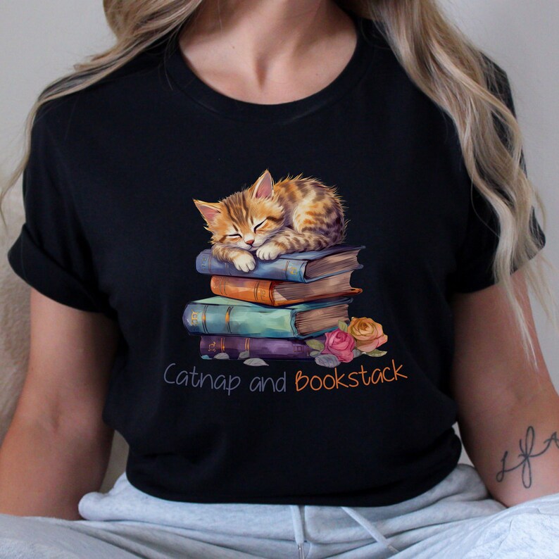 May include: A black t-shirt with a cute cartoon of a tabby cat sleeping on a stack of books. The text "Catnap and Bookstack" is printed below the cat.