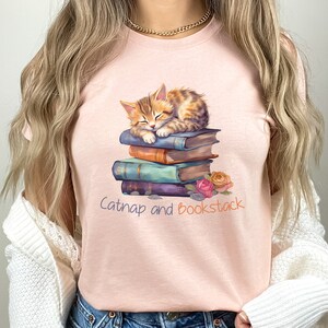 May include: A pink t-shirt with a graphic of a cat napping on a stack of books. The text "Catnap and Bookstack" is printed below the image.