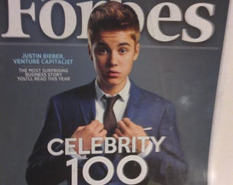 Op de afbeelding: Een magazine cover met de titel "Forbes" en de afbeelding van Justin Bieber. De cover bevat de tekst "Celebrity 100" en andere koppen. De achtergrond is donkerblauw.