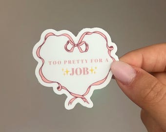 Può includere: Un adesivo bianco con un bordo a nastro rosa e un fiocco in alto. Il testo "TOO PRETTY FOR A JOB" è scritto in rosa, con due stelle dorate. L'adesivo è tenuto in mano.