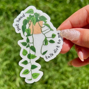Puede incluir: Una pegatina blanca con una planta en maceta con hojas y enredaderas verdes. La maceta es de color marrón claro. La pegatina tiene el texto "pot head talk dirt to me" en negro, curvado alrededor de la planta.