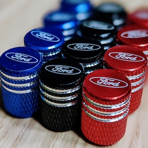 May include: Assortment of valve stem caps with the word "Ford" printed in white on a black, blue, or red background.