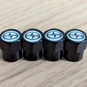 May include: Four black tire valve stem caps with a white Scion logo.