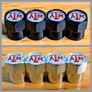 May include: Set of eight tire valve stem caps. Four are black with a white and maroon "ATM" logo, and four are silver with the same logo. The caps are hexagonal and appear to be made of metal.
