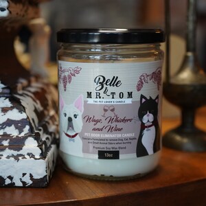 May include: A glass jar candle with a white label featuring a cartoon dog and cat. The label reads "Belle & Mr. Tom The Pet Lover's Candle Wags, Whiskers and Wine Pet Odor Eliminator Candle  Specially formulated to remove Dog, Cat, Reptile and Small Animal Odors when burning Premium Soy Wax Blend 13oz".