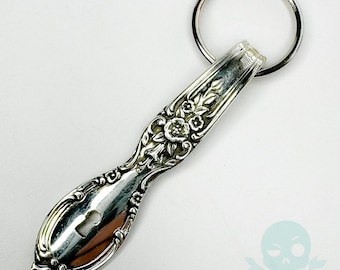 May include: Silver spoon keychain with a floral design and a keyhole cutout. The spoon is attached to a silver ring.